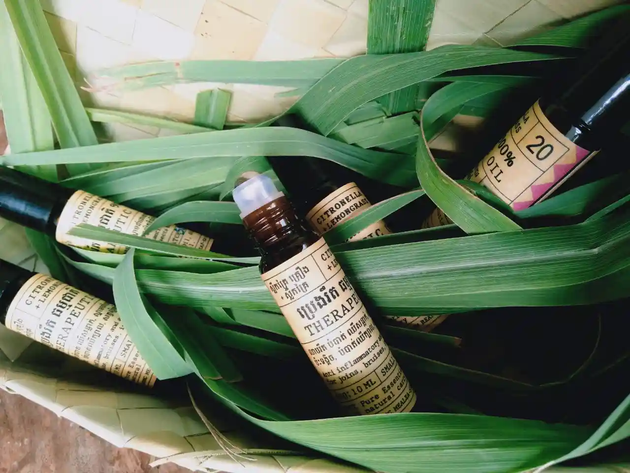 Herbal Kulen citronella and lemongrass therapeutic oil bottles displayed among fresh green leaves.