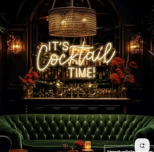Elegant cocktail bar with a green velvet sofa and an illuminated “It’s Cocktail Time” sign.