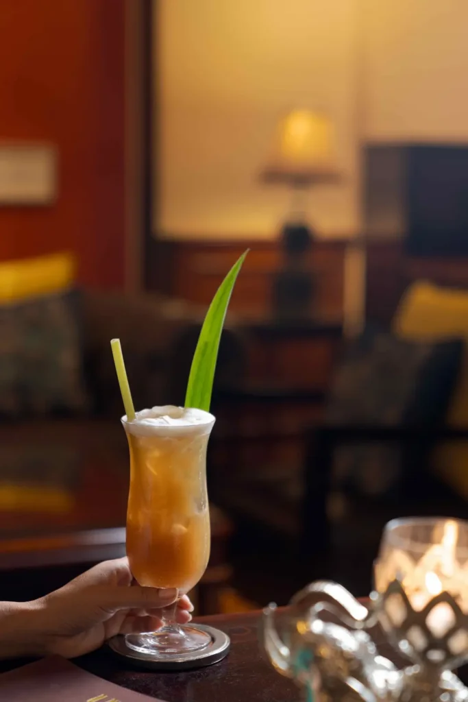 Grand d’Angkor Sling cocktail with Herbal Kulen gin, ice, foam and tropical leaf garnish.