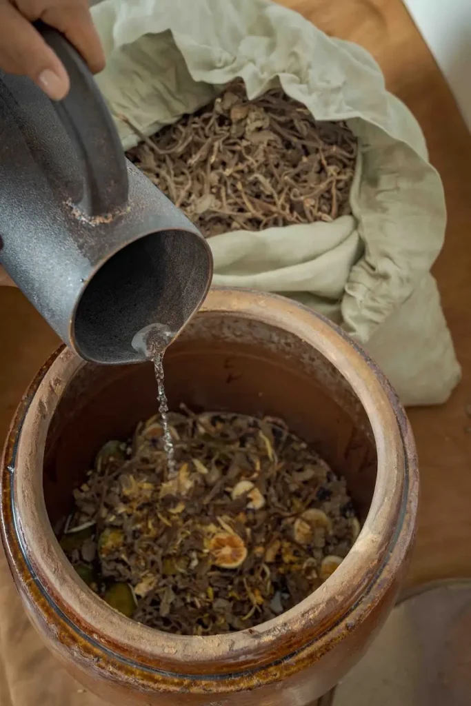 Liquid being poured over dried Cambodian herbs and citrus during the Herbal Kulen gin preparation process.