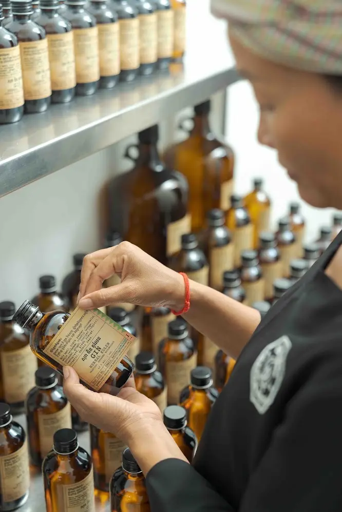 Herbal Kulen distiller applying a label to a small-batch Cambodian gin bottle during production.