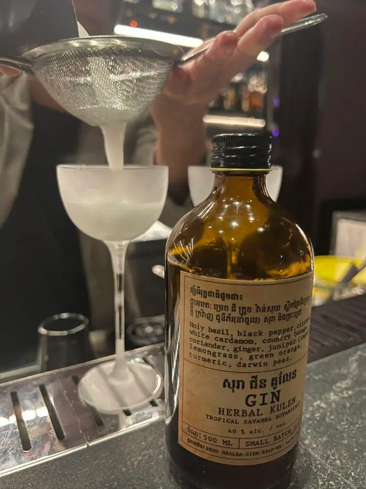 Little Pari cocktail being strained beside a bottle of Herbal Kulen Cambodian gin.